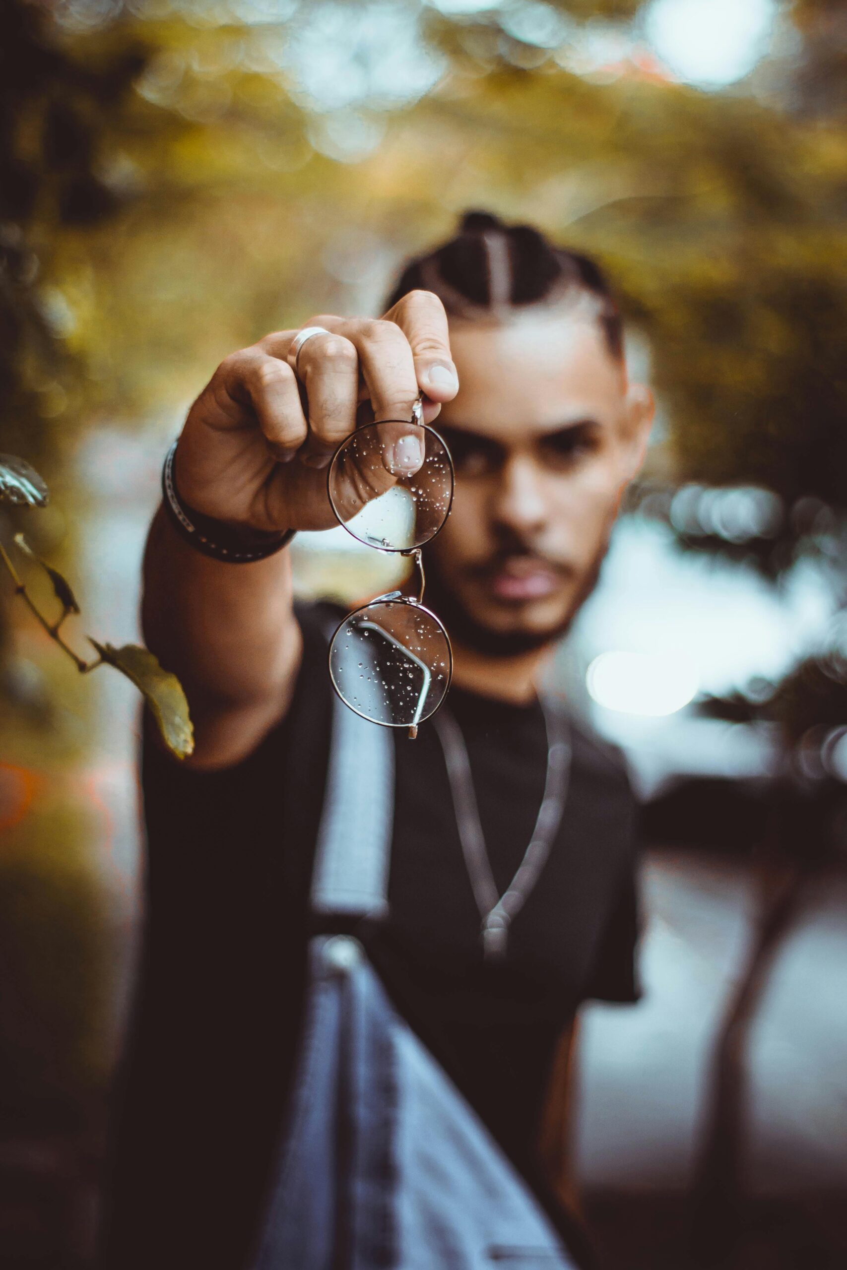 Fashion portrait of a stylish man holding glasses with a blurred bokeh background, showcasing modern eyewear.