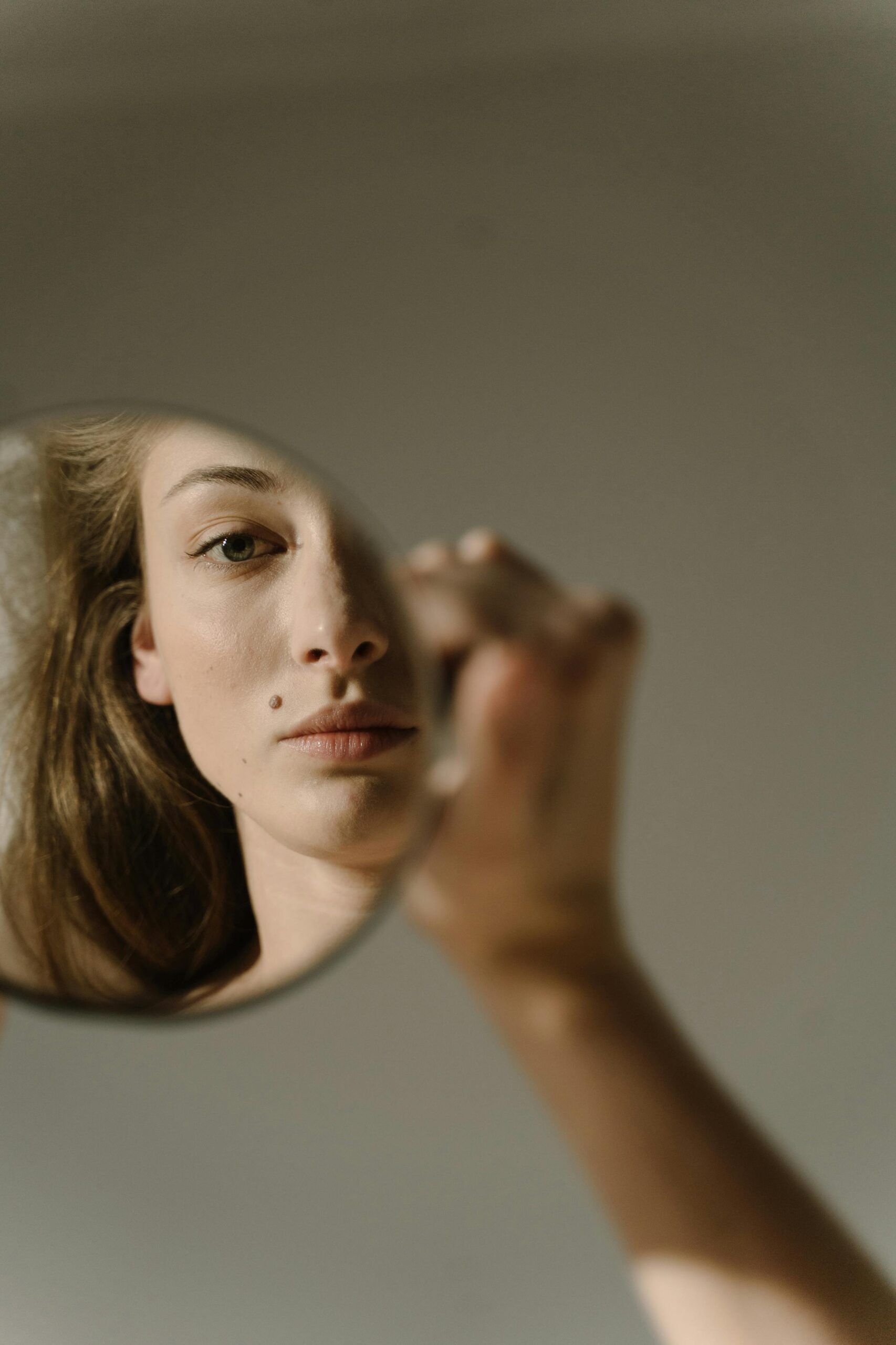 Close-up portrait of a woman looking at her reflection in a round mirror. Soft lighting and selective focus.