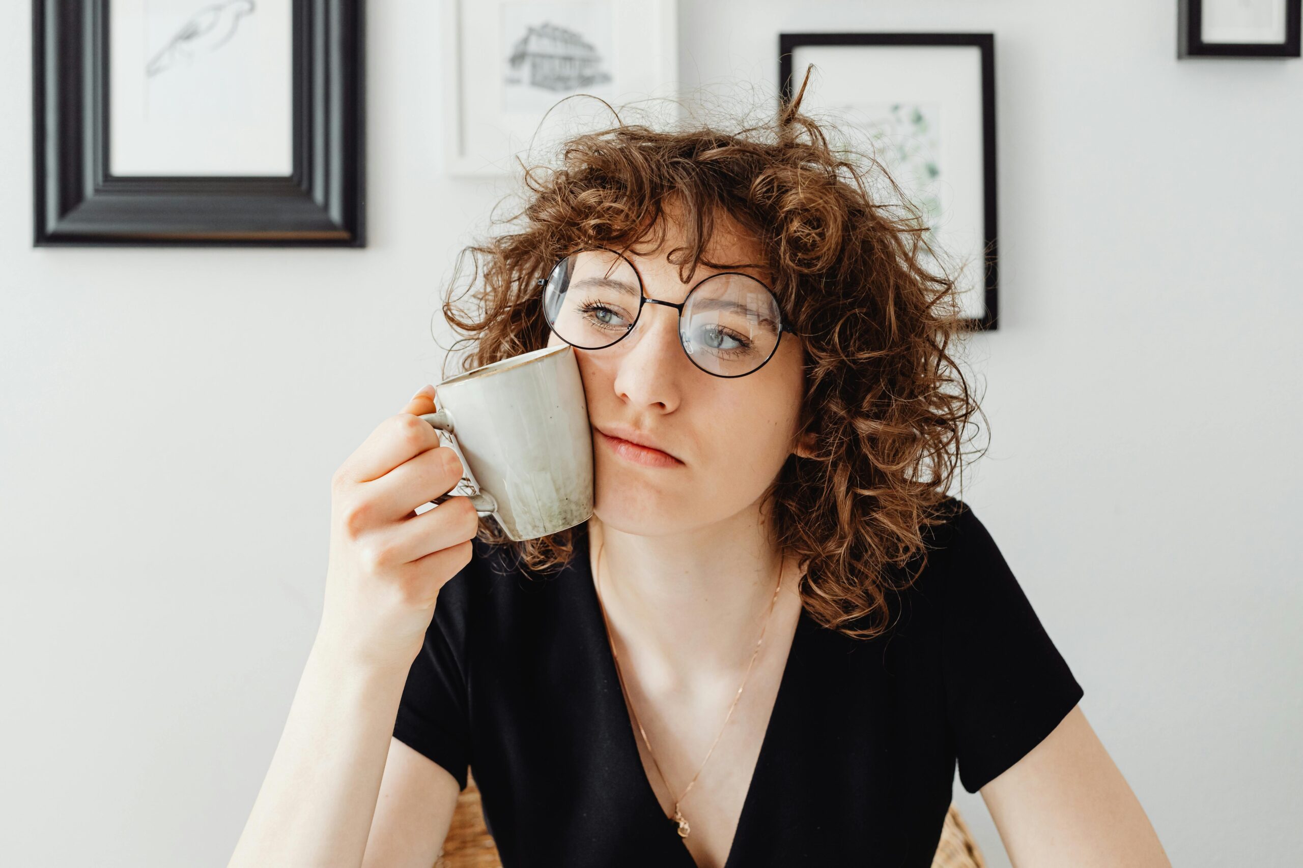 Are You Stuck in Self-Pity Without Even Realizing It? A thoughtful woman with curly hair and glasses holding a coffee mug in a modern room.